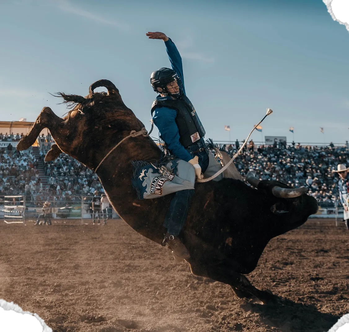 A black bull bucks as its rider leans forward with his hand raised.