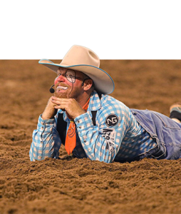 Bullfighter Wacey Munsell in face paint and a cowboy hat, lying in the dirt with his chin in his hands.
