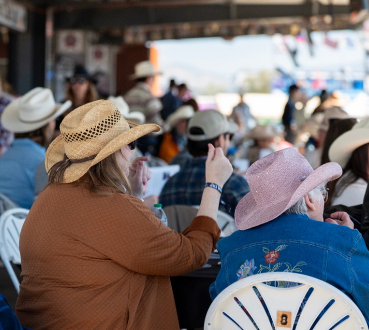 Guests in cowboy hats, one of them pink, at tables under the covered Vaquero Club.
