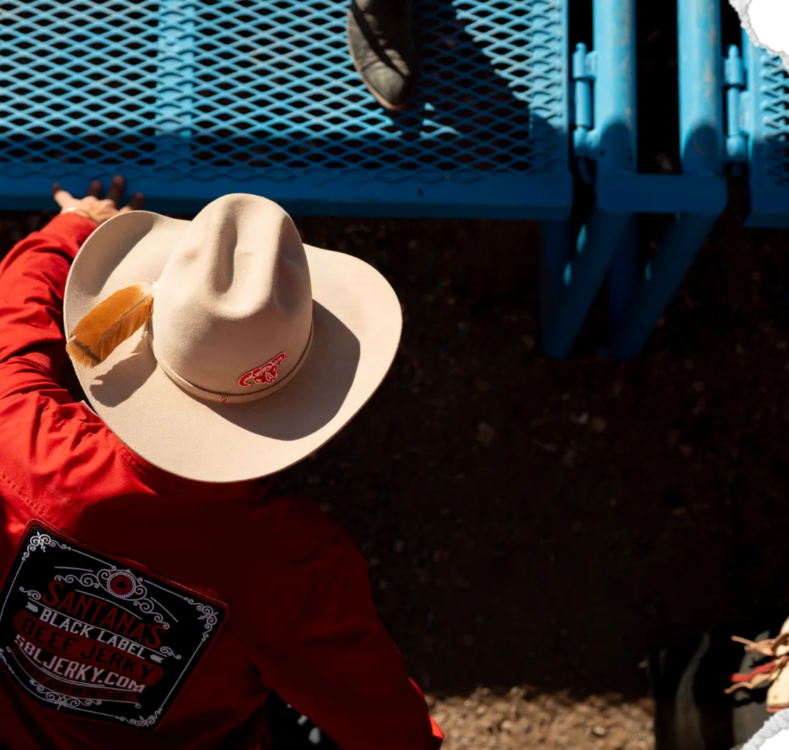 Seen from above, a man in a red shirt and a tan cowboy hat leans on the blue bucking chutes.