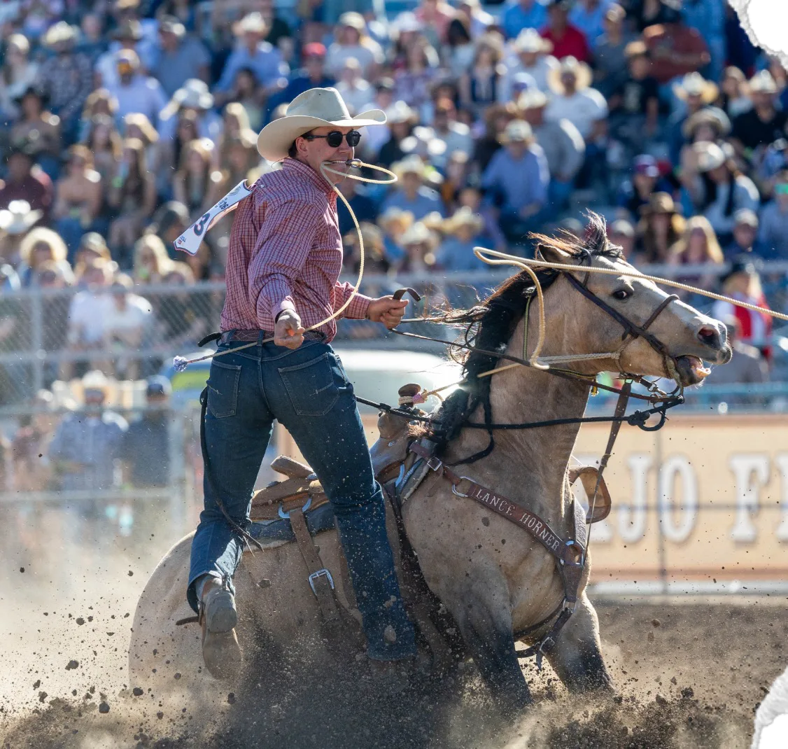 A tie-down roper, piggin' string in his teeth, jumps from his horse.